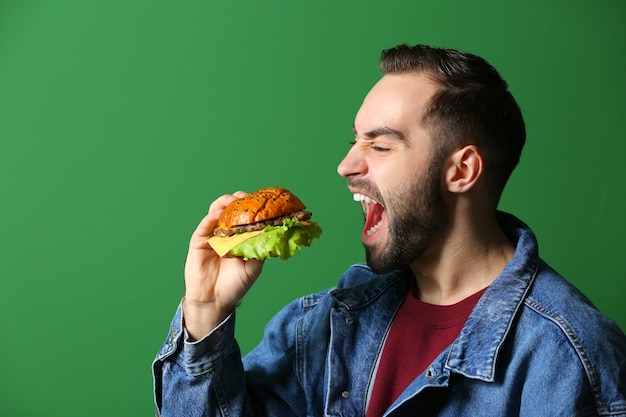 Uomo che mangia hamburger gustoso su verde