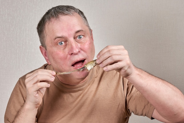 Uomo che mangia pesce fritto che tiene il pesce con le mani davanti al viso