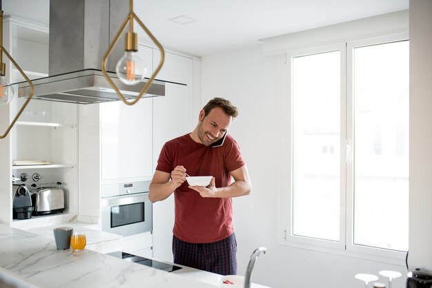 Uomo che mangia prima colazione con il telefono cellulare