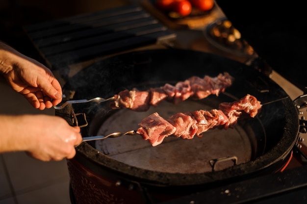 Uomo che mette un grosso pezzo di carne sullo spiedino alla griglia