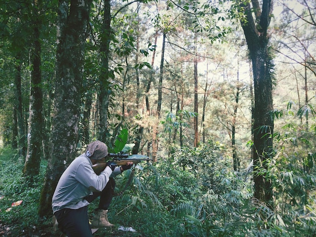 Uomo che mira al fucile mentre è accovacciato nella foresta
