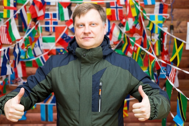 Uomo che mostra i pollici in classe sullo sfondo di un muro di bandiere del mondo.