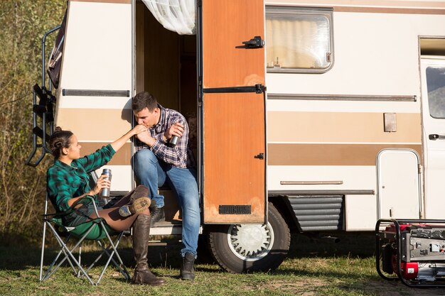 Uomo che mostra il suo amore per la sua ragazza davanti al loro camper retrò baciandole la mano.