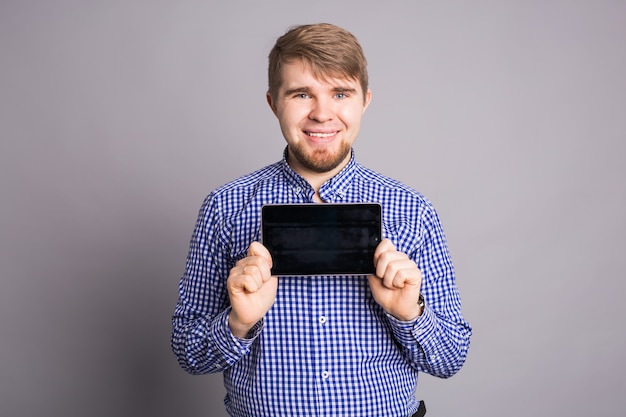 Uomo che mostra lo schermo vuoto il tablet sul muro grigio.