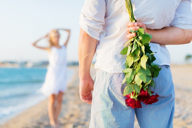 Uomo che nasconde un mazzo di rose da una donna in riva al mare