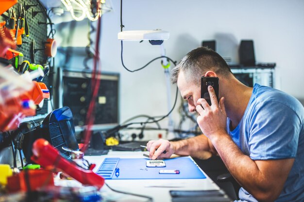 Uomo che parla al cellulare mentre ripara l'elettronica nel negozio di assistenza e manutenzione