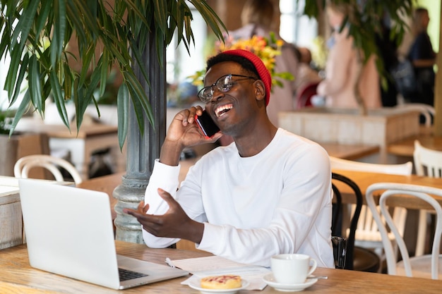 Uomo che parla al telefono con il portatile sul tavolo al caffè