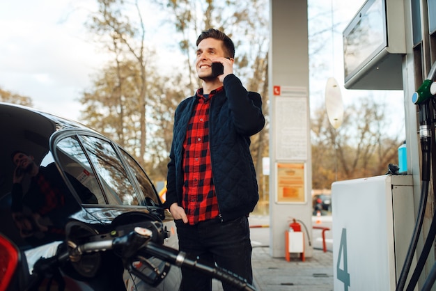 Uomo che parla al telefono e alimenta il veicolo sulla stazione di servizio, rifornimento di carburante. Servizio di rifornimento benzina, benzina o gasolio