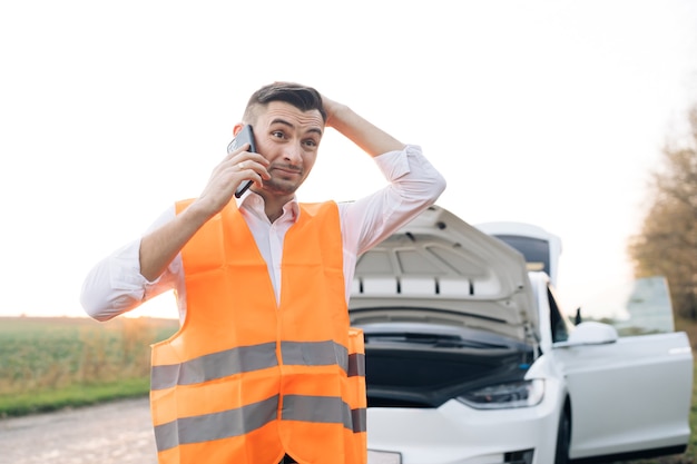 Uomo che parla al telefono e guarda il motore dell'auto