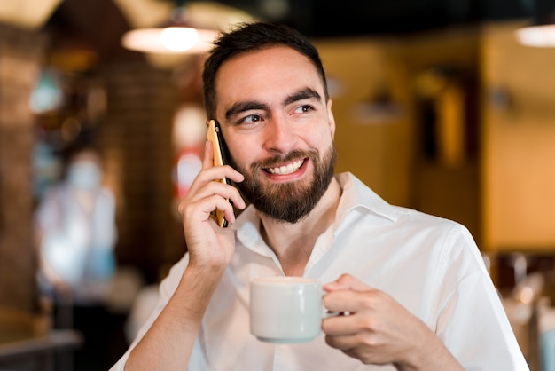 Uomo che parla al telefono mentre beve una tazza di caffè in una caffetteria.