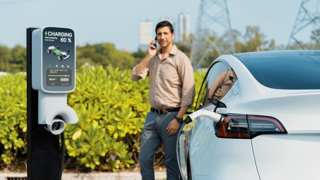 Uomo che parla al telefono mentre ricarica l'auto elettrica alla stazione di ricarica