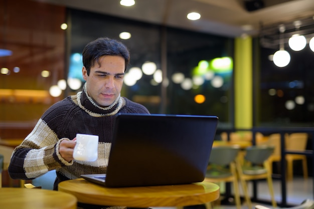 Uomo che per mezzo del computer portatile alla caffetteria