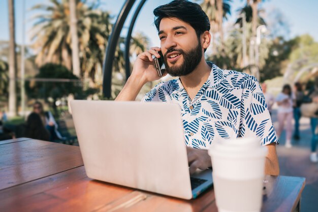 Uomo che per mezzo del suo computer portatile e parlando al telefono.