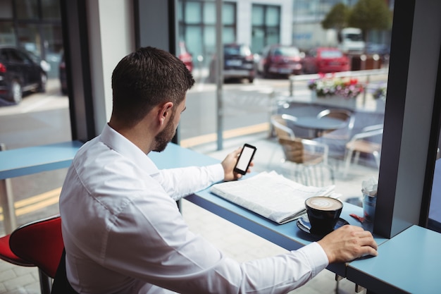 Uomo che per mezzo del telefono cellulare mentre mangiando caffè