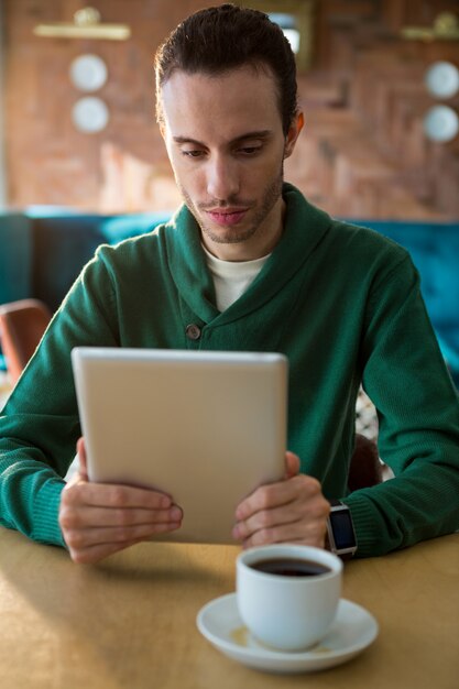 Uomo che per mezzo della compressa digitale e della tazza di caffè sulla tavola