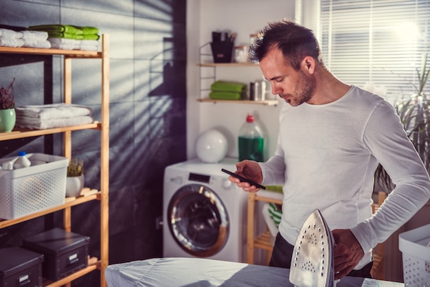 Uomo che per mezzo dello Smart Phone mentre stirando i vestiti