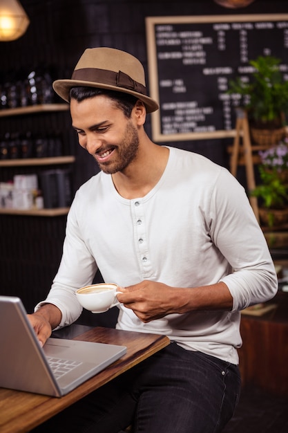 Uomo che per mezzo di un computer portatile e bevendo caffè