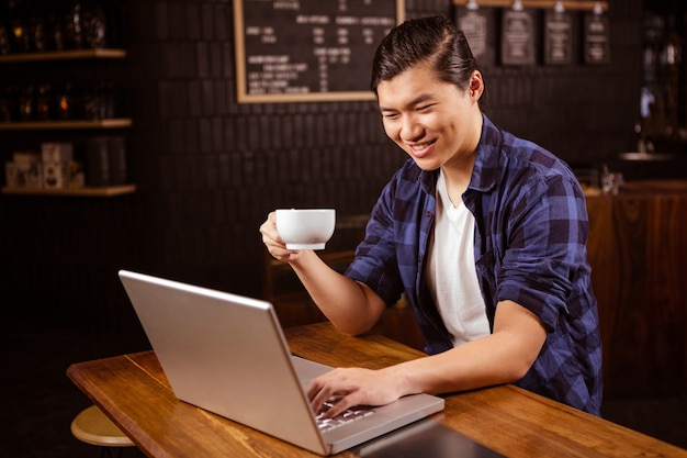 Uomo che per mezzo di un computer portatile e bevendo caffè