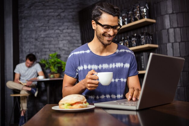 Uomo che per mezzo di un computer portatile e bevendo caffè