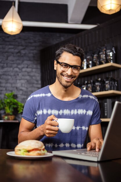 Uomo che per mezzo di un computer portatile e bevendo caffè