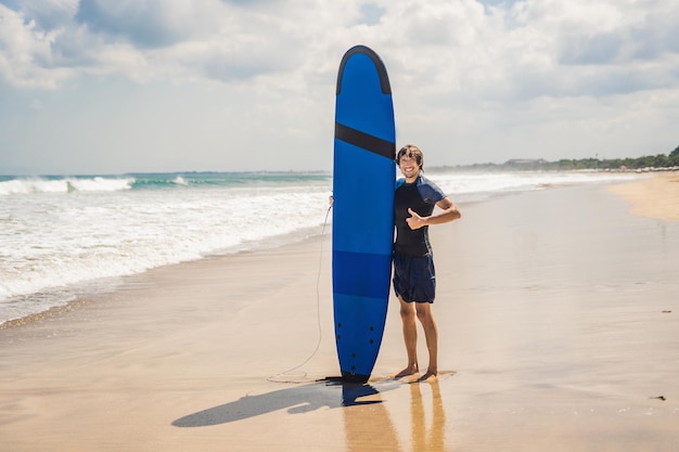 Uomo che porta la tavola da surf sopra la sua testa. Primo piano di un bel ragazzo con la tavola da surf sulla testa in spiaggia. Ritratto di uomo che porta la tavola da surf sulla testa nascosta e sorridente in spiaggia