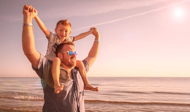 Uomo che porta su di sé il figlio mentre è in piedi sulla spiaggia contro il cielo durante il tramonto