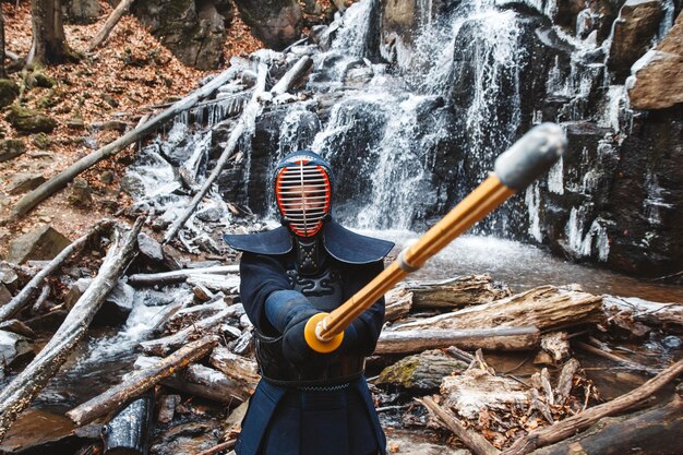 Uomo che pratica il kendo con la spada di bambù sulle rocce della cascata e sullo sfondo della foresta