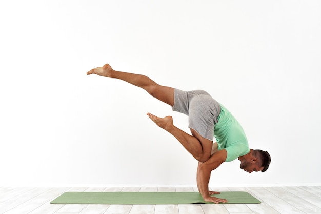 Uomo che pratica la posa di yoga dell'equilibrio su studio bianco