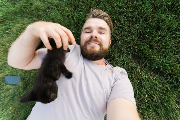 Uomo che prende selfie con lo smartphone con il piccolo gattino sdraiato e che gioca sull'erba amicizia ama gli animali e il concetto di proprietario dell'animale domestico