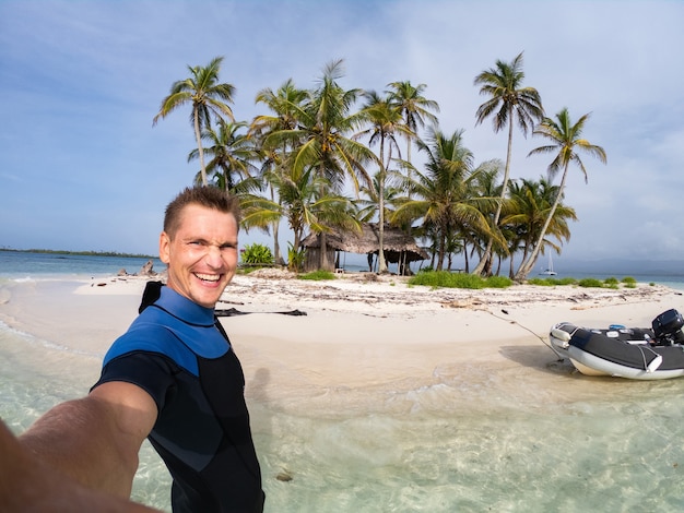 Uomo che prende selfie su una piccola isola tropicale con palme da cocco e spiaggia di sabbia bianca. Avventura e concetto di viaggio.