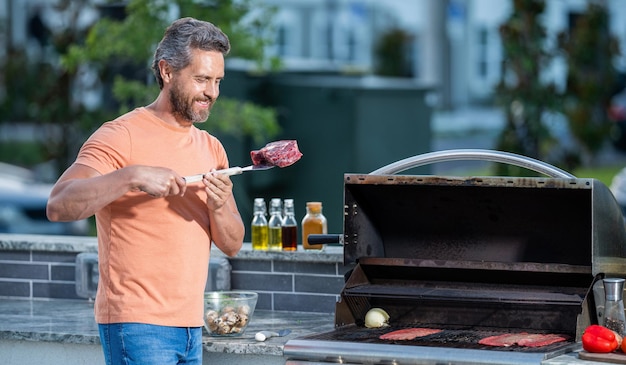 Uomo che prepara cibo alla griglia al barbecue in giardino uomo con griglia calda a una festa barbecue uomo che griglia un delizioso barbecue in una giornata estiva Sfrigolante bistecca di controfiletto alla griglia