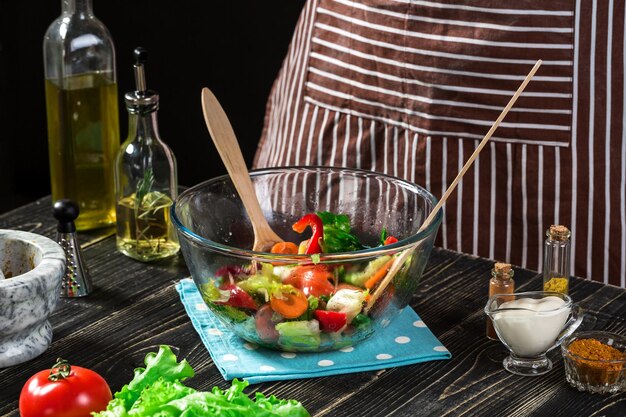 Uomo che prepara insalata con verdure fresche su un tavolo di legno. Cucinare cibi gustosi e sani. Su sfondo nero. Cibo vegetariano, concetto sano o di cucina.