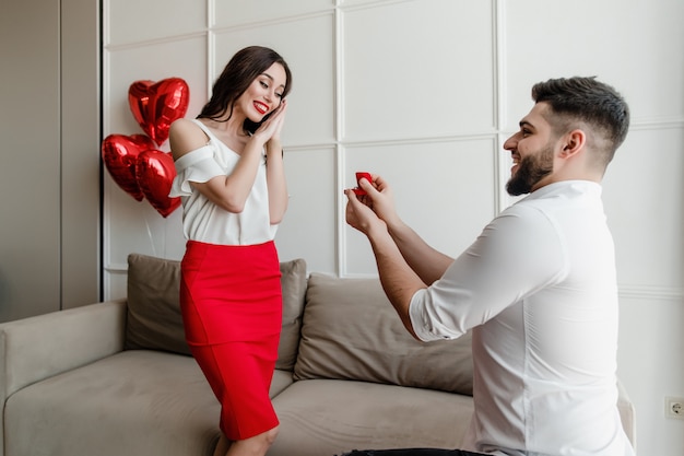 Uomo che propone di fidanzare con un anello e palloncini a forma di cuore a casa in appartamento