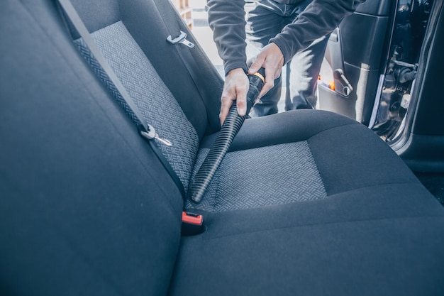 Uomo che pulisce, aspira l'interno dell'auto con un aspirapolvere, concetto di trasporto