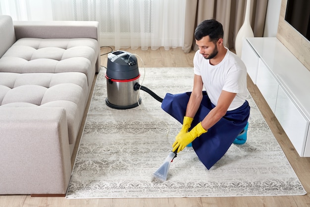 Uomo che pulisce il tappeto nel soggiorno utilizzando l'aspirapolvere a casa.