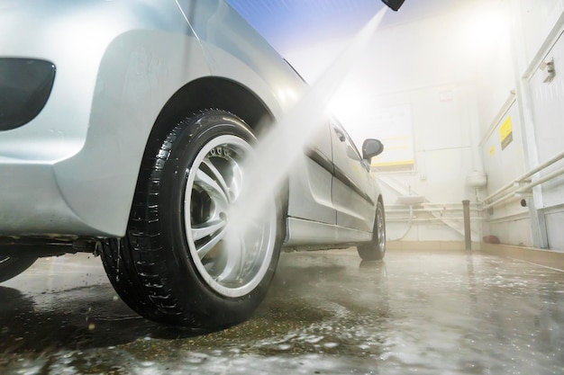 Uomo che pulisce il veicolo con getto d'acqua ad alta pressione o getto Dettagli dell'autolavaggio che lavano la ruota posteriore di un'auto