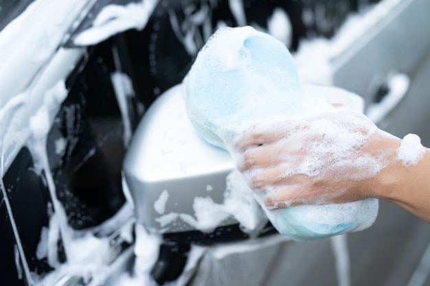 Uomo che pulisce l'auto nera con una spugna blu