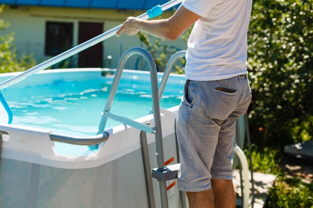 uomo che pulisce la piscina nella sua casa di campagna. Concetto di estate a casa. Stile di vita