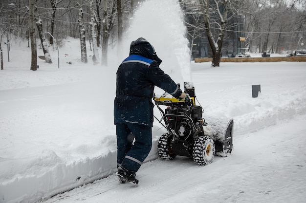Uomo che pulisce o rimuove la neve con uno spazzaneve su una strada innevata nel parco