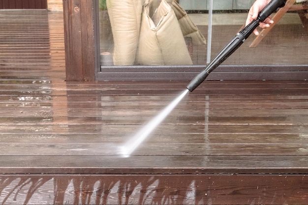 Uomo che pulisce pareti e pavimenti con idropulitrice ad alta pressione Lavaggio assi di legno per terrazze e pareti di rivestimento