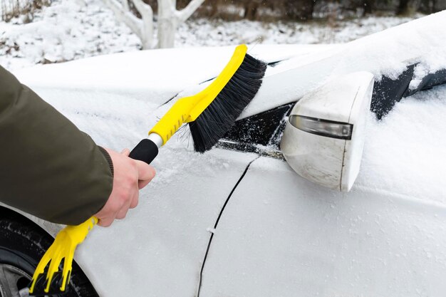 Uomo che raschia la neve dall'auto specchietto retrovisore con spazzola Persona che pulisce la neve fresca dopo la tempesta di neve