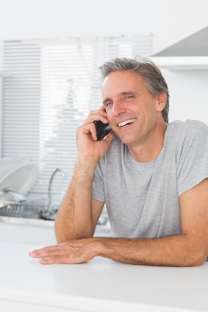 Uomo che ride facendo una telefonata in cucina