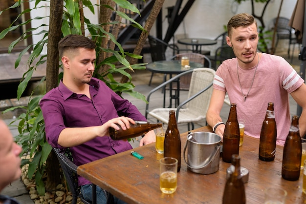 Uomo che riempie il bicchiere di birra mentre gli amici parlano e si siedono