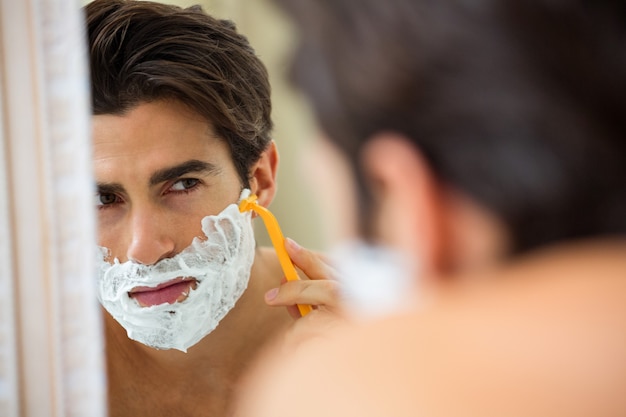 Uomo che riflette nello specchio mentre si rade la barba