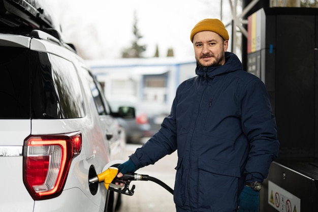 Uomo che rifornisce di carburante la sua auto SUV americana alla stazione di servizio quando fa freddo