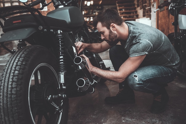 Uomo che ripara la bici. Fiducioso giovane che ripara motocicletta vicino al suo garage