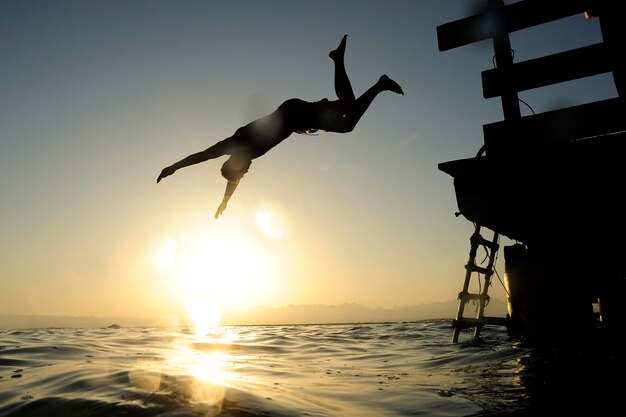 Uomo che salta dal molo in mare al tramonto