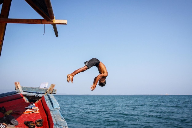 Uomo che salta dalla barca in mare contro un cielo limpido
