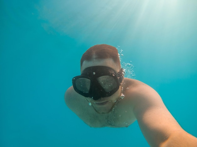 Uomo che scatta foto selfie sott'acqua in maschera subacquea