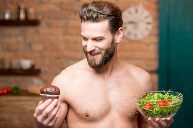 Uomo che sceglie tra muffin dolci e insalata in cucina